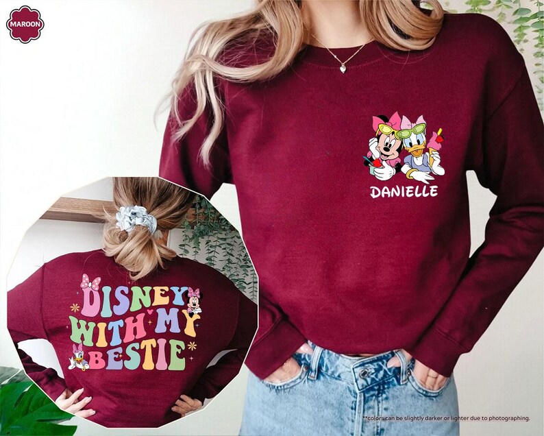 May include: A maroon long-sleeved sweatshirt with a colorful graphic on the back that says "DISNEY WITH MY BESTIE" and a graphic of Minnie Mouse and Daisy Duck on the front with the name "DANIELLE" underneath.