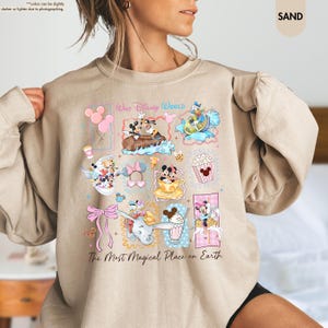 May include: Sand-colored sweatshirt featuring colorful Disney character graphics. The design includes Mickey and Minnie Mouse, Donald Duck, and Dumbo, with the text "Walt Disney World" and "The Most Magical Place on Earth."