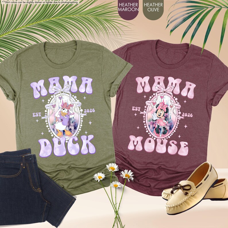May include: Two heathered t-shirts, one olive green and one maroon, with the text "MAMA DUCK" and "MAMA MOUSE" in lavender and pink, respectively. Each shirt features a cartoon character design and the text "EST 2026".