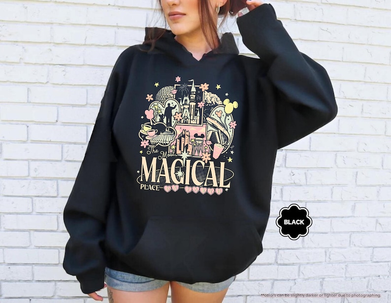 May include: Black hooded sweatshirt with a colorful graphic featuring a castle, Mickey Mouse ears, and the text "The Most Magical Place." The design includes pink, yellow, and black elements. The sweatshirt has a front pocket.