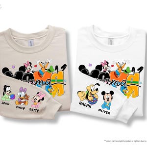 K&ouml;nnte beinhalten: Zwei lang&auml;rmlige Sweatshirts, eines in Sandfarbe und eines in Wei&szlig;, mit einem Disney-Motiv. Das Design enth&auml;lt das Wort "Mama" mit Disney-Figuren und Namen wie John, Emily, Betty, Ralph und Oliver. Die Sweatshirts sind gefaltet.