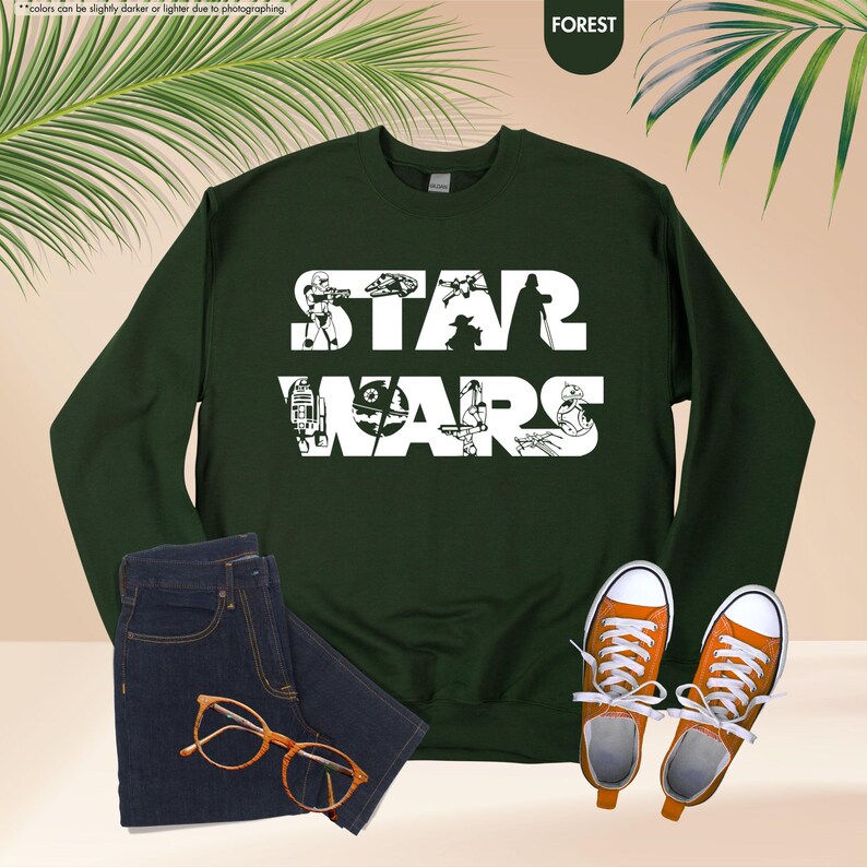 May include: A forest green sweatshirt with the words "STAR WARS" in white, featuring character silhouettes. The image includes a pair of dark wash jeans, orange sneakers, and eyeglasses.