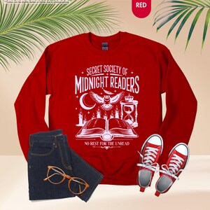 May include: A red sweatshirt with the text "SECRET SOCIETY OF MIDNIGHT READERS" and a graphic of an owl, candles, and an open book. The image also includes blue jeans, glasses, and red sneakers.