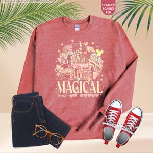 May include: Heather scarlet red sweatshirt with a graphic that says "The Most Magical Place on Earth". The image also includes a pair of dark wash jeans, red sneakers, and eyeglasses.