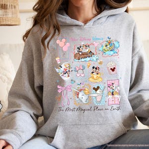 May include: Sport grey hoodie featuring a colorful collage of Disney characters and icons. The design includes Mickey and Minnie Mouse, Donald Duck, and Dumbo, with the text "Walt Disney World" and "The Most Magical Place on Earth".