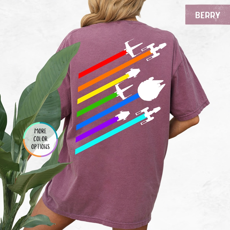 K&ouml;nnte beinhalten: Ein lila T-Shirt mit einem Regenbogenmuster und wei&szlig;en Silhouetten von Star Wars Raumschiffen. Der Text "BERRY" befindet sich in der oberen rechten Ecke des Bildes.