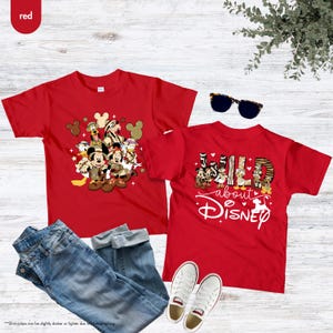 May include: Two red t-shirts featuring Disney characters. One shirt displays a group of characters, while the other says "Wild about Disney." Blue jeans, white sneakers, and sunglasses are also in the image.