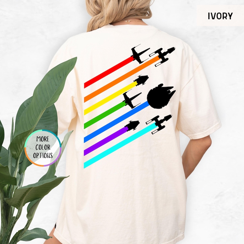 K&ouml;nnte beinhalten: Ein wei&szlig;es T-Shirt mit einem Regenbogenmuster und Silhouetten von Star Wars Raumschiffen. Der Text "IVORY" befindet sich in der oberen rechten Ecke des Bildes.