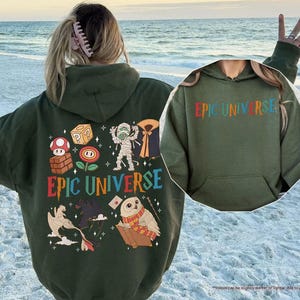 May include: A military green hoodie with the text "EPIC UNIVERSE" in colorful letters. The back of the hoodie features various cartoon graphics, including a mushroom, a cube, a mummy, and an owl reading a book.