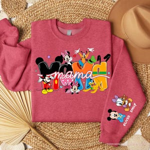K&ouml;nnte beinhalten: Ein rotes Sweatshirt mit dem Wort "Mama" in einem farbenfrohen Design mit Mickey Mouse, Minnie Mouse, Goofy und anderen Disney-Figuren. Der &Auml;rmel tr&auml;gt die Namen "Oliver" und "Emily" mit Disney-Figuren.