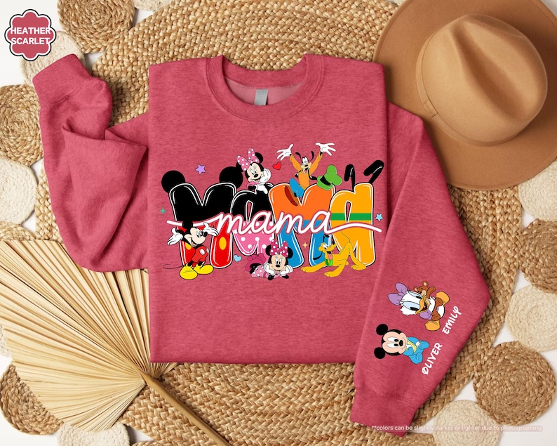 K&ouml;nnte beinhalten: Ein rotes Sweatshirt mit dem Wort "Mama" in einem farbenfrohen Design mit Mickey Mouse, Minnie Mouse, Goofy und anderen Disney-Figuren. Der &Auml;rmel tr&auml;gt die Namen "Oliver" und "Emily" mit Disney-Figuren.