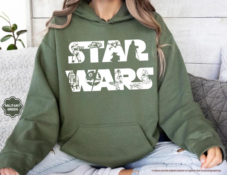 May include: Military green hoodie with a white "STAR WARS" graphic. The graphic features iconic characters and elements from the Star Wars franchise. The hoodie has a front pocket and a drawstring hood.