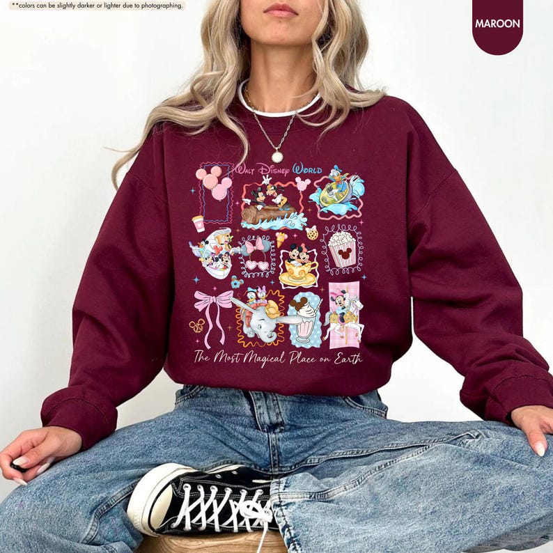 May include: Maroon sweatshirt featuring a colorful graphic of Disney World characters and attractions. The design includes Mickey Mouse, Dumbo, and other iconic elements. Text on the sweatshirt reads "Walt Disney World" and "The Most Magical Place on Earth."