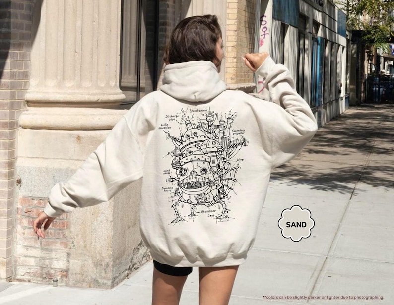 May include: A cream-colored hoodie with a black and white illustration of a flying machine on the back. The illustration includes text labels for different parts of the machine. The text "SAND" is in a circle on the bottom right corner of the hoodie.
