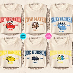 Puede incluir: Seis camisetas de color crema con diferentes personajes de la pel&iacute;cula Cars. Cada camiseta tiene el nombre de un personaje en negrita, un gr&aacute;fico de coche y el texto "Cars" debajo. Las camisetas est&aacute;n dispuestas sobre una estera tejida.