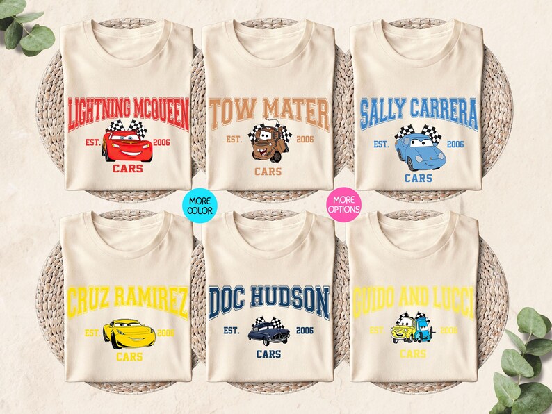Puede incluir: Seis camisetas de color crema con diferentes personajes de la pel&iacute;cula Cars. Cada camiseta tiene el nombre de un personaje en negrita, un gr&aacute;fico de coche y el texto "Cars" debajo. Las camisetas est&aacute;n dispuestas sobre una estera tejida.