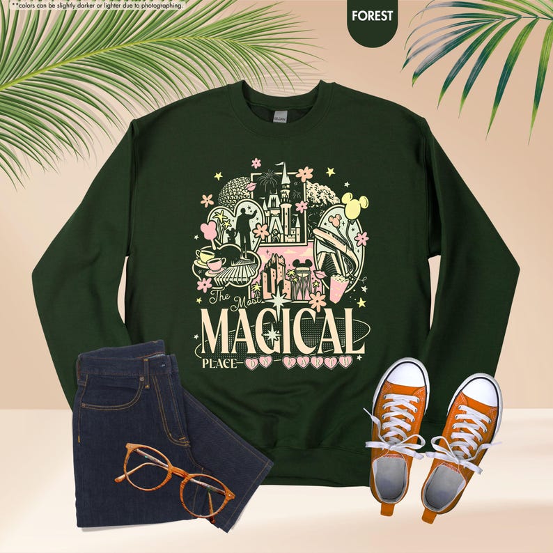 May include: Forest green sweatshirt with a colorful graphic that reads "The Most Magical Place." The graphic includes a castle, Mickey Mouse, and other theme park elements. Paired with blue jeans, orange sneakers, and glasses.