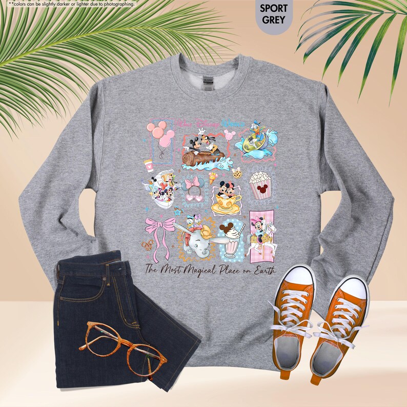 May include: Sport grey sweatshirt featuring colorful Disney character illustrations. The design includes Mickey and Minnie Mouse, Donald Duck, and other characters. The text "The Most Magical Place on Earth" is printed below the illustrations. Paired with blue jeans and orange sneakers.
