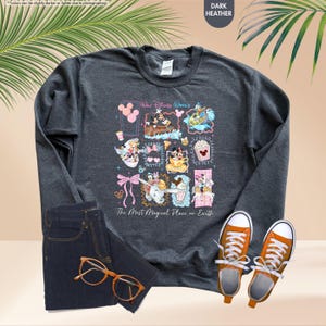 May include: Dark heather gray sweatshirt featuring a colorful graphic of Disney characters and the text "Walt Disney World" and "The Most Magical Place on Earth." The sweatshirt is paired with dark wash jeans and orange sneakers.