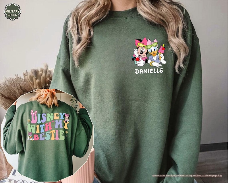 May include: A green sweatshirt with a colorful graphic of Disney characters Mickey Mouse and Minnie Mouse. The text "DISNEY WITH MY BESTIE" is printed on the back of the sweatshirt. The text "DANIELLE" is printed on the front of the sweatshirt.