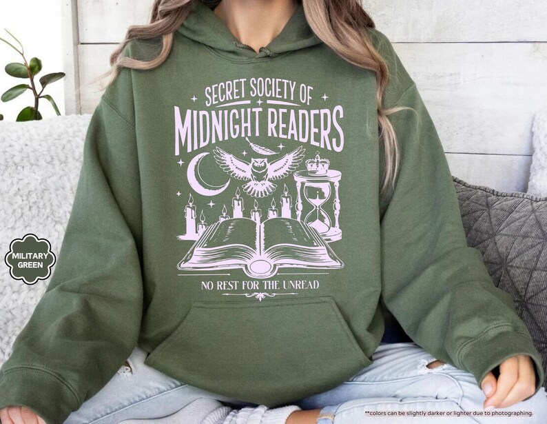May include: Military green hoodie with a front graphic that reads "SECRET SOCIETY OF MIDNIGHT READERS" with an owl, moon, candles, and an open book. The text "NO REST FOR THE UNREAD" is below the graphic. The hoodie has a kangaroo pocket.