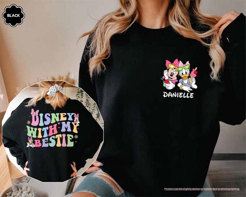 May include: Black sweatshirt with a colorful graphic of Disney characters Minnie Mouse and Daisy Duck wearing sunglasses and holding drinks. The text "Disney with my bestie" is on the back of the sweatshirt. The name "Danielle" is printed below the characters.