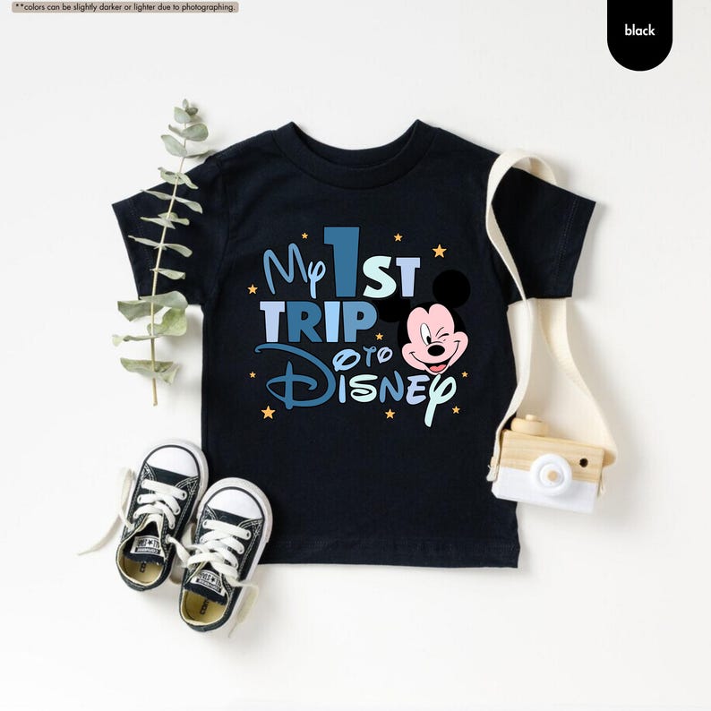 K&ouml;nnte beinhalten: Schwarzes T-Shirt mit einer blauen und wei&szlig;en Grafik, auf der "My 1st Trip to Disney" mit einem Cartoon-Mickey-Mouse-Kopf steht.