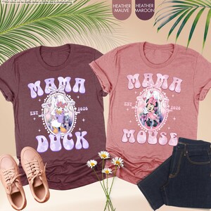 May include: Two heather t-shirts with the word "MAMA" in a bubble font. One shirt is maroon with a Daisy Duck graphic, the other is mauve with a Minnie Mouse graphic. Both shirts have "EST 2026" below the graphics.