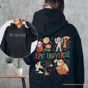 May include: Black hoodie with the text "EPIC UNIVERSE" in rainbow colors on the front and back. The back features colorful cartoon graphics of a mummy, owl, and other fantasy elements.