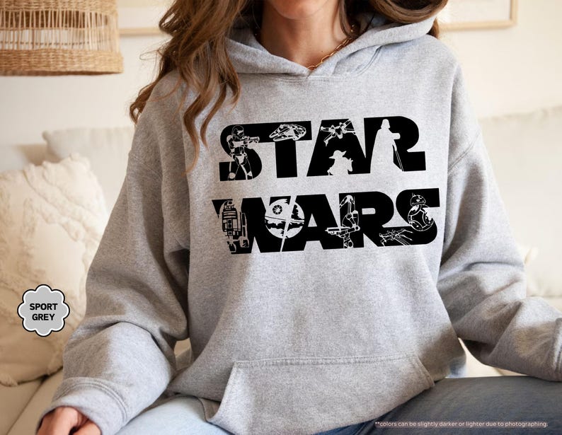 May include: A light grey hoodie with the words "STAR WARS" in large black letters. The letters are filled with black silhouettes of characters and vehicles from the Star Wars franchise. The hoodie has a front pocket and a hood.