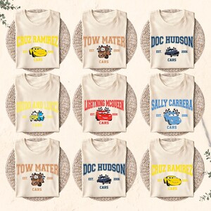 Puede incluir: Nueve camisetas color crema con varios personajes de la pel&iacute;cula Cars. Cada camiseta muestra el nombre de un personaje, un gr&aacute;fico de coche y la palabra "CARS". Las camisetas est&aacute;n dispuestas sobre manteles individuales tejidos.