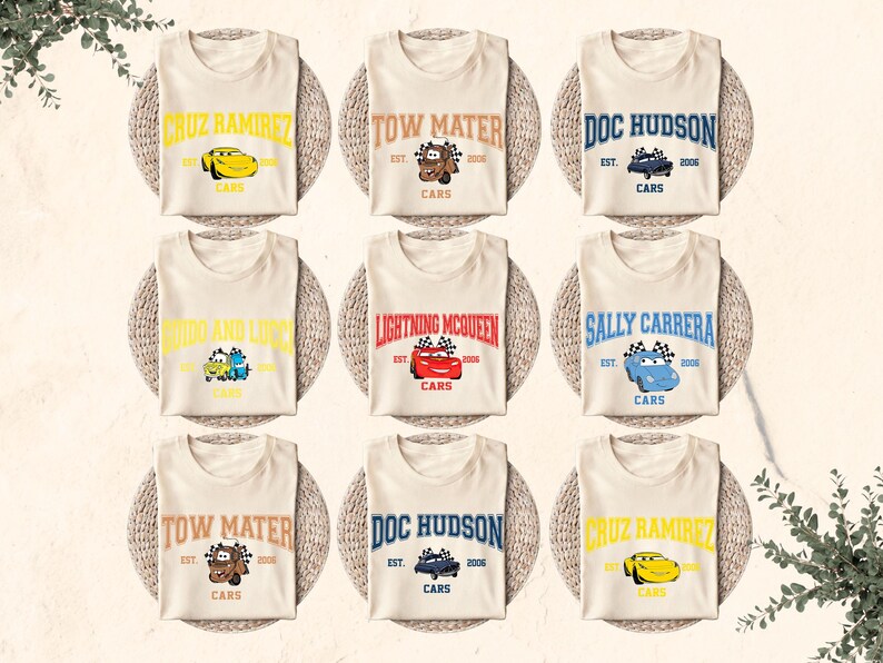 Puede incluir: Nueve camisetas color crema con varios personajes de la pel&iacute;cula Cars. Cada camiseta muestra el nombre de un personaje, un gr&aacute;fico de coche y la palabra "CARS". Las camisetas est&aacute;n dispuestas sobre manteles individuales tejidos.