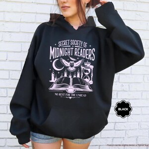 May include: Black hooded sweatshirt with a white graphic that reads "SECRET SOCIETY OF MIDNIGHT READERS" with an owl, moon, and open book design. The text "NO REST FOR THE UNREAD" is also included. The sweatshirt has a front pocket.
