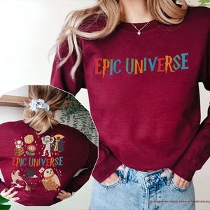 May include: A maroon sweatshirt with the text "EPIC UNIVERSE" in colorful letters. The back of the sweatshirt features various cartoon characters and the same text. The sweatshirt is a long-sleeved, crew neck style.