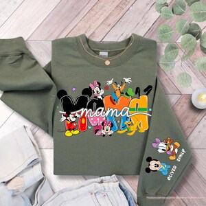 K&ouml;nnte beinhalten: Olivgr&uuml;nes Sweatshirt mit dem Wort "Mama" in farbenfrohen Disney-Buchstaben. Mit Micky, Minnie, Donald und Goofy. Der &Auml;rmel zeigt die Namen "Oliver" und "Emily" mit Micky und Daisy.