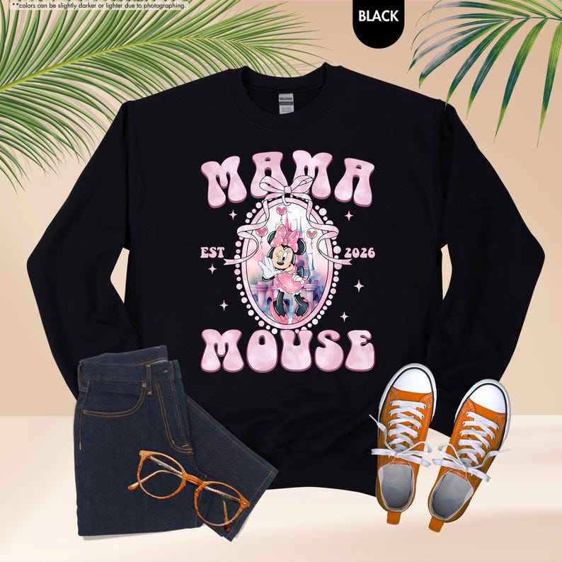 May include: Black sweatshirt with the text "MAMA MOUSE EST 2026" in pink, featuring a Minnie Mouse graphic. The image includes blue jeans, orange eyeglasses, and orange sneakers.