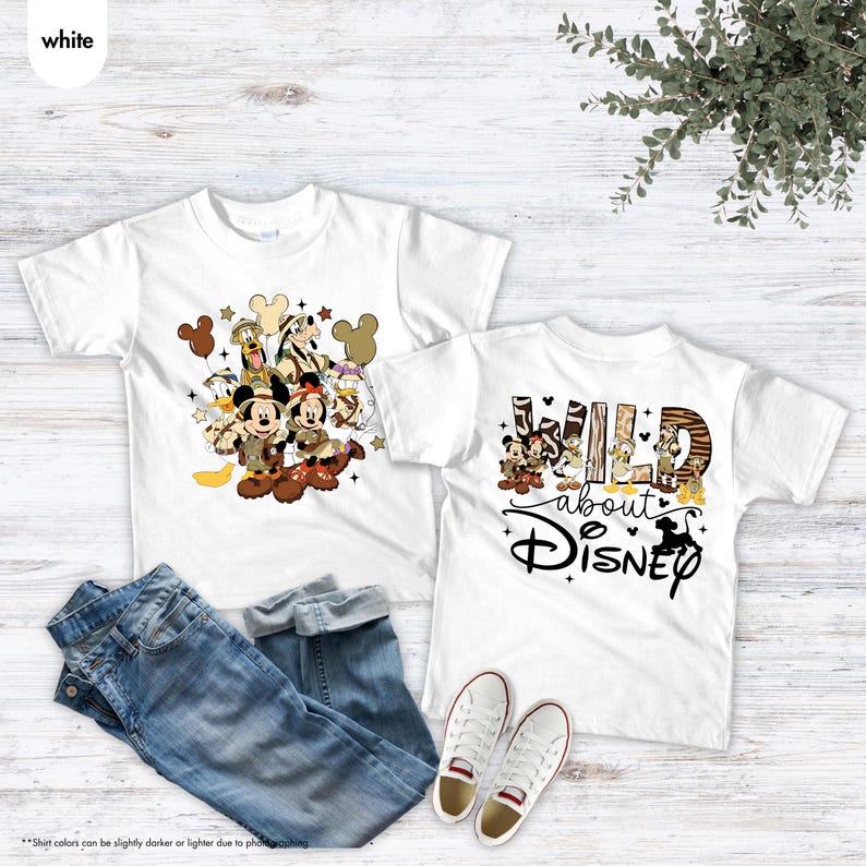 May include: Two white t-shirts with Disney character graphics. One shirt features Mickey and Minnie Mouse, Donald Duck, and Goofy. The other shirt says "Wild about Disney" with Disney characters. Blue jeans and white sneakers are also in the image.