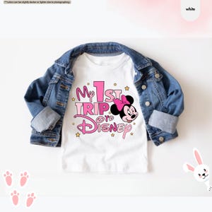 K&ouml;nnte beinhalten: Wei&szlig;es T-Shirt mit einer pinkfarbenen und wei&szlig;en Grafik mit der Aufschrift "My 1st Trip to Disney" und einem Cartoon-Bild von Minnie Mouse.