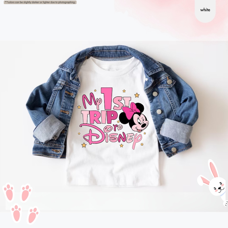K&ouml;nnte beinhalten: Wei&szlig;es T-Shirt mit einer pinkfarbenen und wei&szlig;en Grafik mit der Aufschrift "My 1st Trip to Disney" und einem Cartoon-Bild von Minnie Mouse.