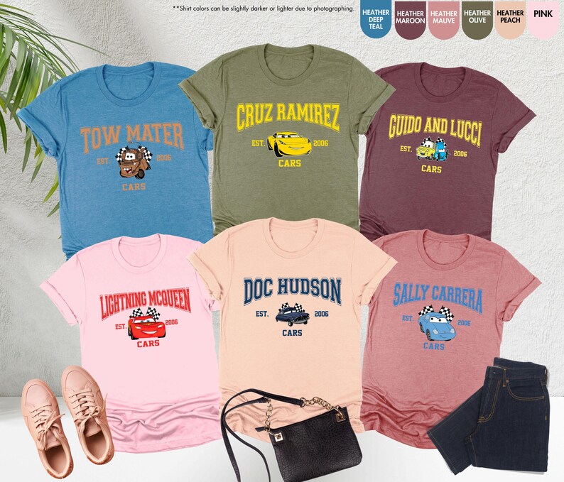Puede incluir: Varias camisetas con tem&aacute;tica de Cars en varios colores, cada una con el nombre de un personaje y gr&aacute;ficos. Las camisetas incluyen Tow Mater, Cruz Ramirez, Guido y Lucci, Lightning McQueen, Doc Hudson y Sally Carrera. La imagen tambi&eacute;n incluye zapatillas deportivas, un bolso y vaqueros.