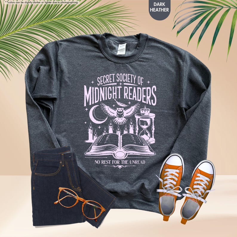 May include: Dark heather gray sweatshirt with the text "SECRET SOCIETY OF MIDNIGHT READERS" in white. The graphic includes an owl, candles, an hourglass, and an open book. The sweatshirt is paired with dark blue jeans and orange sneakers.