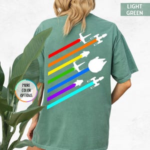 K&ouml;nnte beinhalten: Ein hellgr&uuml;nes T-Shirt mit einem Regenbogenmuster und wei&szlig;en Silhouetten von Star Wars Raumschiffen. Der Text "LIGHT GREEN" befindet sich in der oberen rechten Ecke des Bildes.