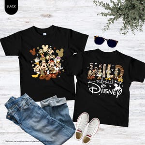 May include: Two black t-shirts with Disney character graphics. One shirt features Mickey and Minnie Mouse, Donald Duck, and other characters. The other shirt says "Wild About Disney" with a Dalmatian silhouette. Blue jeans and white sneakers are also in the image.