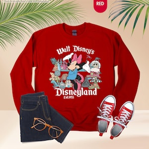 May include: A red sweatshirt with the text "Walt Disney's Disneyland Est. 1955" and a graphic of Minnie Mouse. The image also includes a pair of blue jeans, red sneakers, and gold-rimmed glasses.