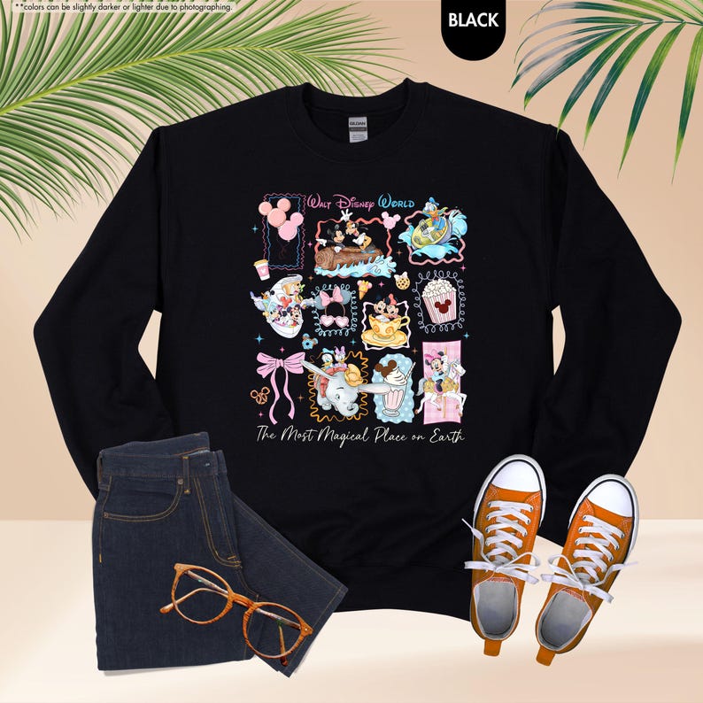 May include: Black long-sleeve sweatshirt with a colorful graphic featuring Disney characters and the text "Walt Disney World" and "The Most Magical Place on Earth." The sweatshirt is paired with blue jeans, orange sneakers, and glasses.
