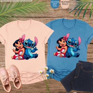 K&ouml;nnte beinhalten: Zwei T-Shirts, eines in Pfirsich und eines in Blau, mit einer Cartoon-Grafik eines M&auml;dchens und eines blauen Au&szlig;erirdischen. Das Pfirsich-Shirt hat passende Turnschuhe. Das blaue Shirt wird mit dunkelblauen Jeans kombiniert. Der Text auf dem Bild lautet: "Die Farben der Shirts k&ouml;nnen aufgrund der Fotografie etwas dunkler oder heller sein."