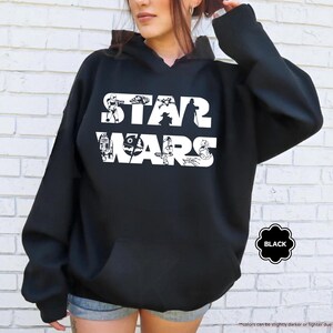 May include: Black hooded sweatshirt with the words "STAR WARS" in white, featuring character illustrations within the letters. The sweatshirt has a drawstring hood and a front pocket. The word "BLACK" is in a black and white circle.