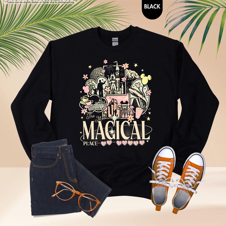 May include: Black long-sleeve sweatshirt with a colorful graphic design featuring a castle, Mickey Mouse, and the text "The Most Magical Place". The sweatshirt is paired with blue jeans, orange glasses, and orange sneakers.