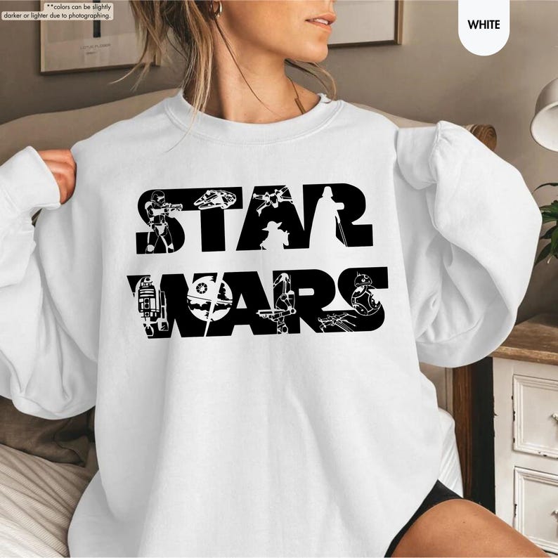 May include: White sweatshirt featuring the text "STAR WARS" in large black letters. The letters are filled with various black and white illustrations of characters and vehicles from the Star Wars franchise. The sweatshirt is a crew neck style.