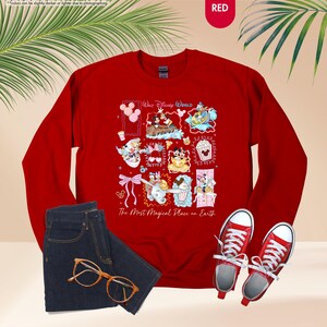 May include: A red sweatshirt featuring a collage of Disney characters and icons, with the text "Walt Disney World" and "The Most Magical Place on Earth." The image also includes a pair of blue jeans, red sneakers, and gold-rimmed glasses.